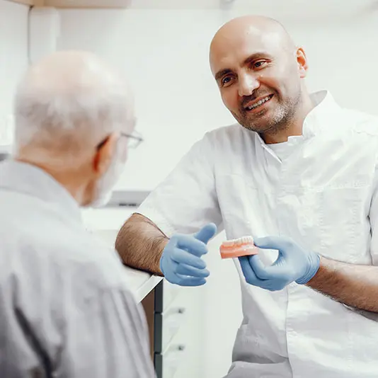 man-talking-to-dentist-holding-dentures-square-534x534px Dental Implants Missing Teeth Dentures Dentist Implant Darwen Lancashire Blackburn Bolton Burnley